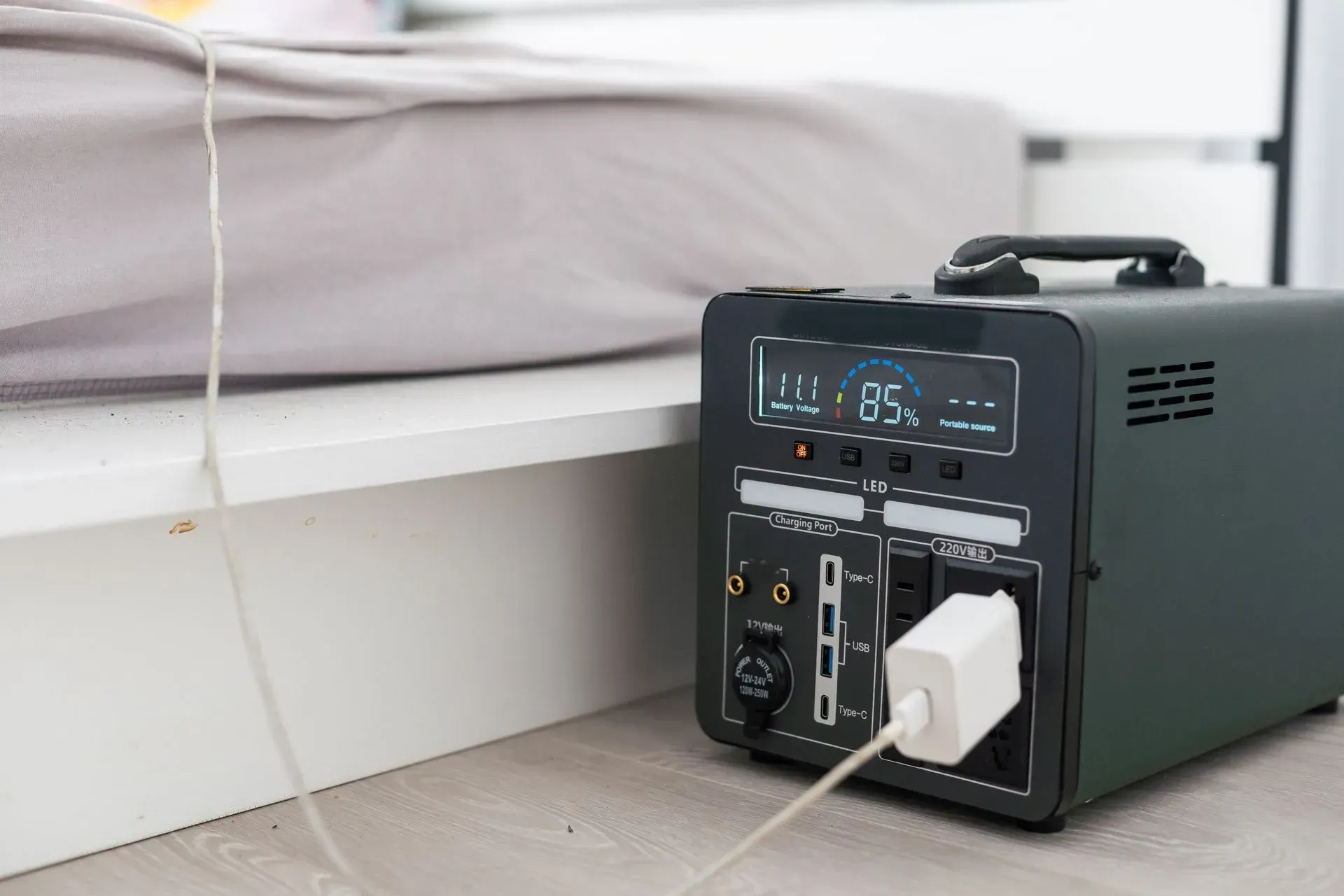 Portable power station charging a white device beside a bed.