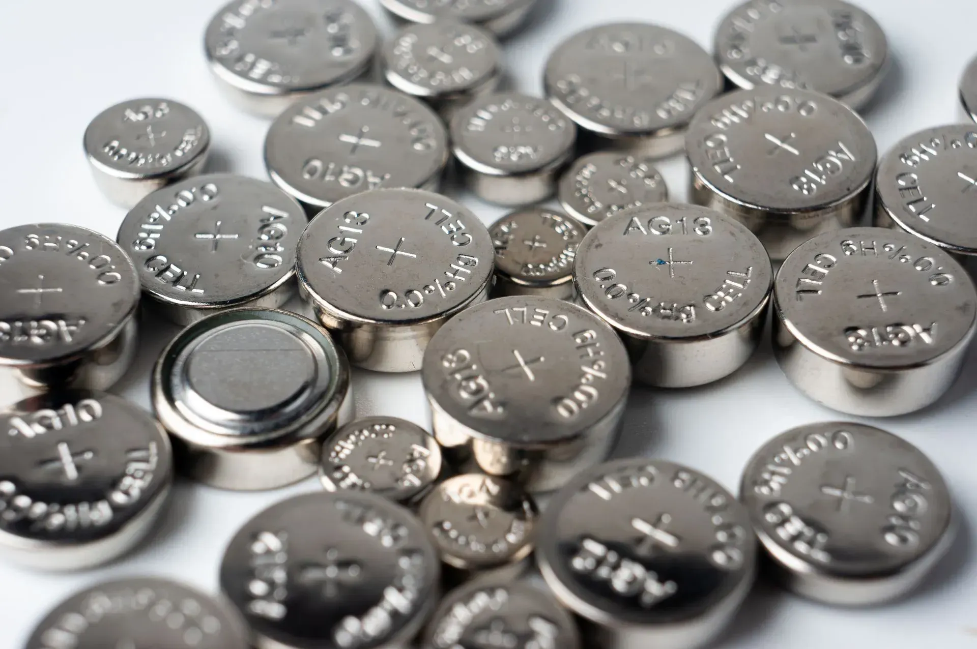 Assorted silver button cell batteries scattered on a white surface