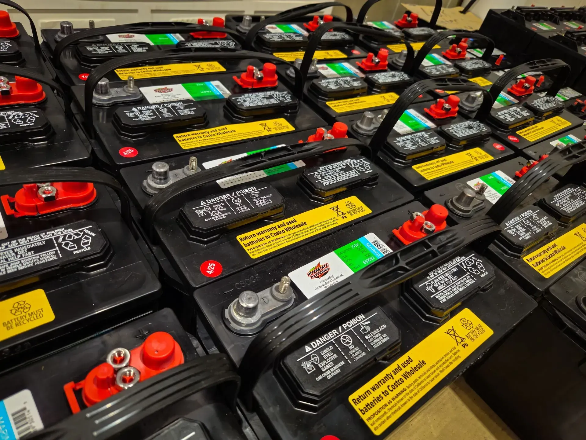 Rows of car batteries with black cases, red terminals, and yellow labels in a storage/display area