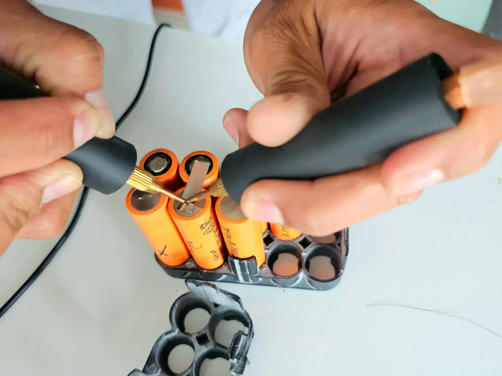 Hands assembling an orange-and-black battery pack with a soldering iron and pliers