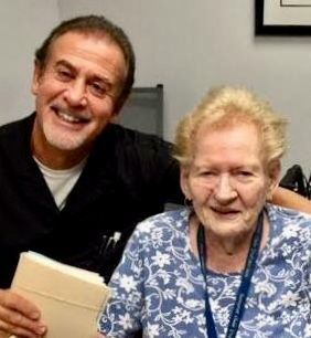 Two people smiling indoors, seated close together in an office setting.