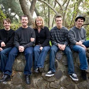 Five people sitting on a rock outdoors in a wooded park, smiling at the camera.