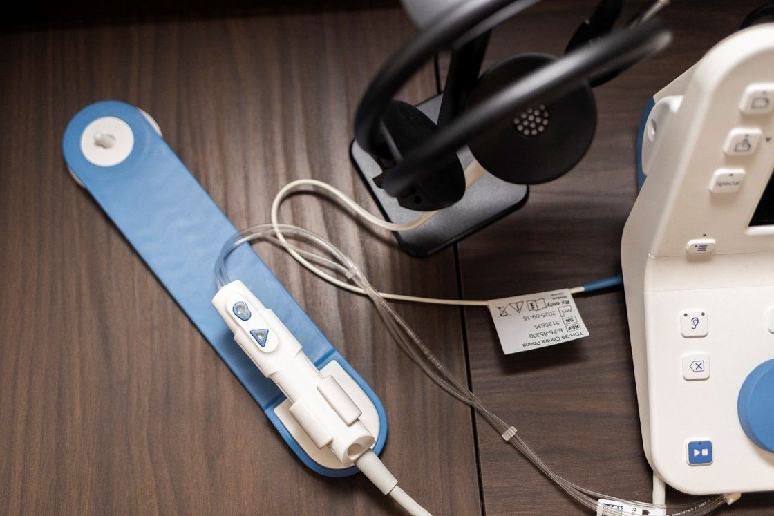Bracciale blu per la misurazione della pressione sanguigna da polso accanto a uno stetoscopio nero e a un monitor medico bianco su una scrivania.