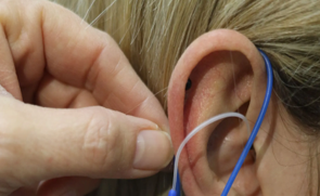 Una mano che regola un apparecchio acustico blu e bianco dietro l'orecchio