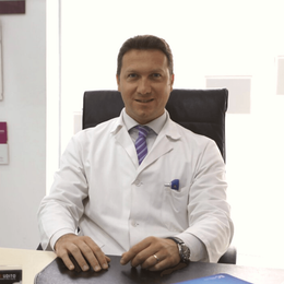 Un medico in camice bianco è seduto a una scrivania e guarda in camera in un ufficio luminoso.