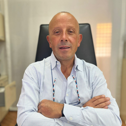 Persona seduta a una scrivania con le braccia incrociate, che indossa una camicia a righe azzurre, in un ambiente d'ufficio.