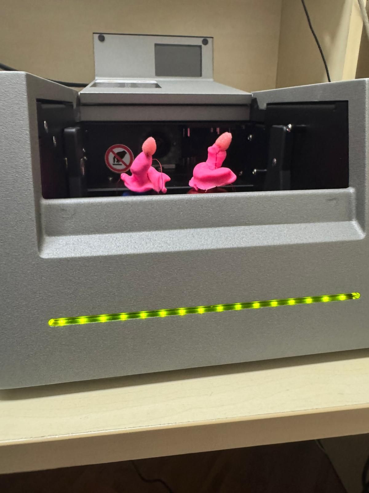 Macchina grigia con due piccole statuette rosa all'interno e una fila di LED gialli sotto.