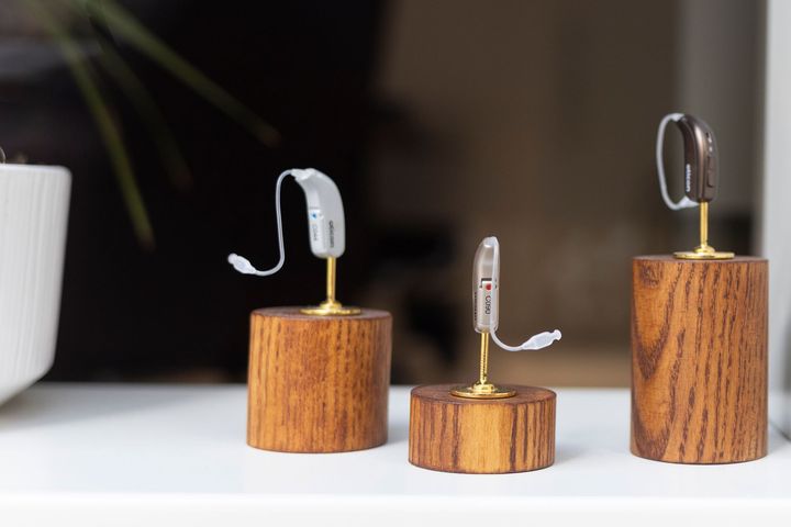 Tre piccoli supporti in legno che reggono auricolari wireless su una superficie bianca.