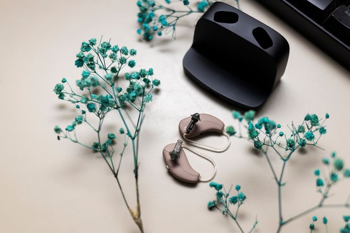 Custodia nera per auricolari wireless e auricolari su una superficie chiara con fiori color verde acqua nelle vicinanze.