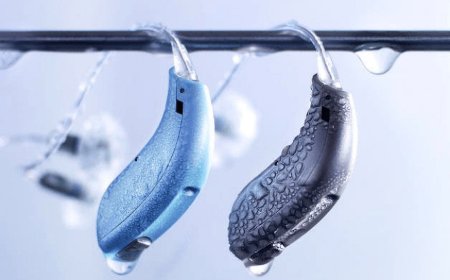 Due apparecchi acustici, uno blu e uno grigio, appesi a un filo metallico con gocce d'acqua.