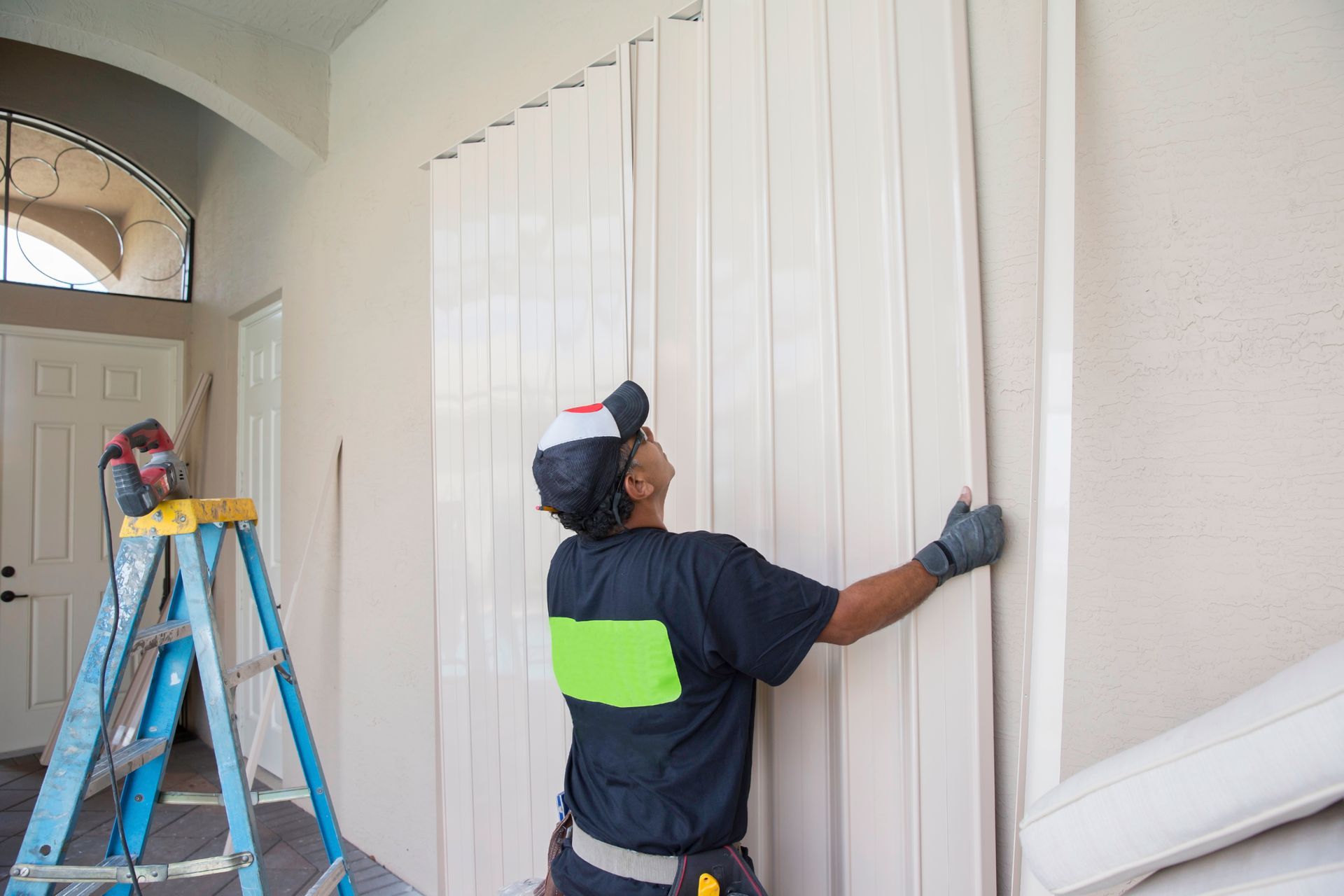 A worker installs hurricane shutters on a home's exterior wall.