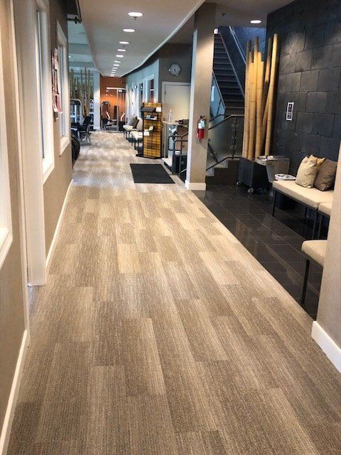 Modern office hallway with wood flooring, lounge seating, and conference areas at the far end