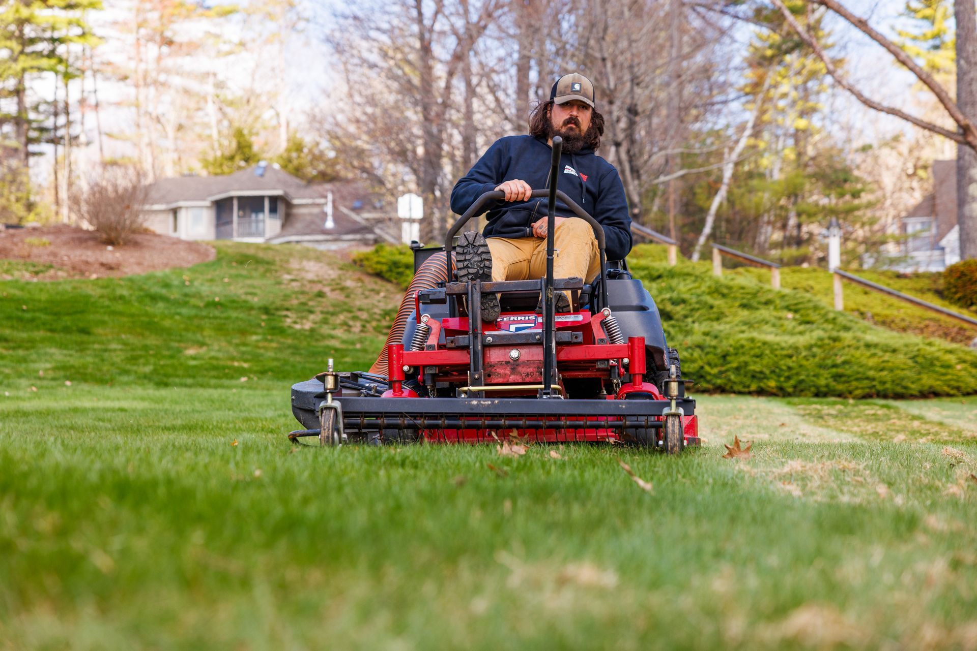 Three workers in green shirts and khaki pants perform landscaping tasks, including trimming a hedge and mowing the lawn.