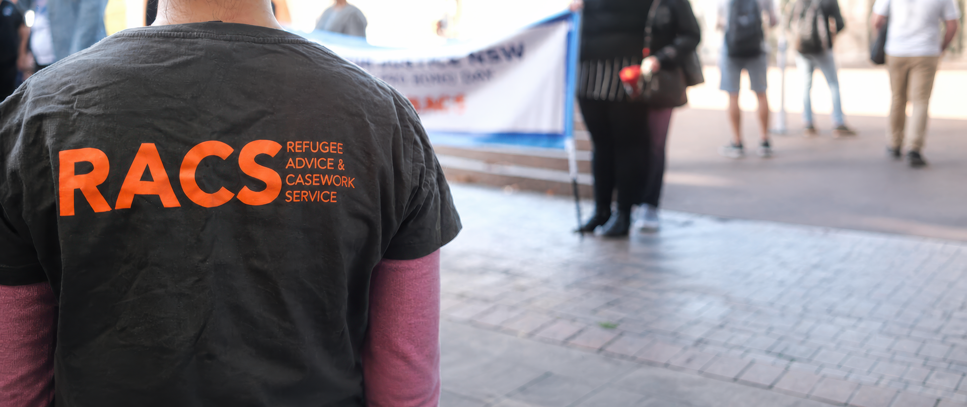 Person wearing a black shirt with orange “RACS” text at an indoor event