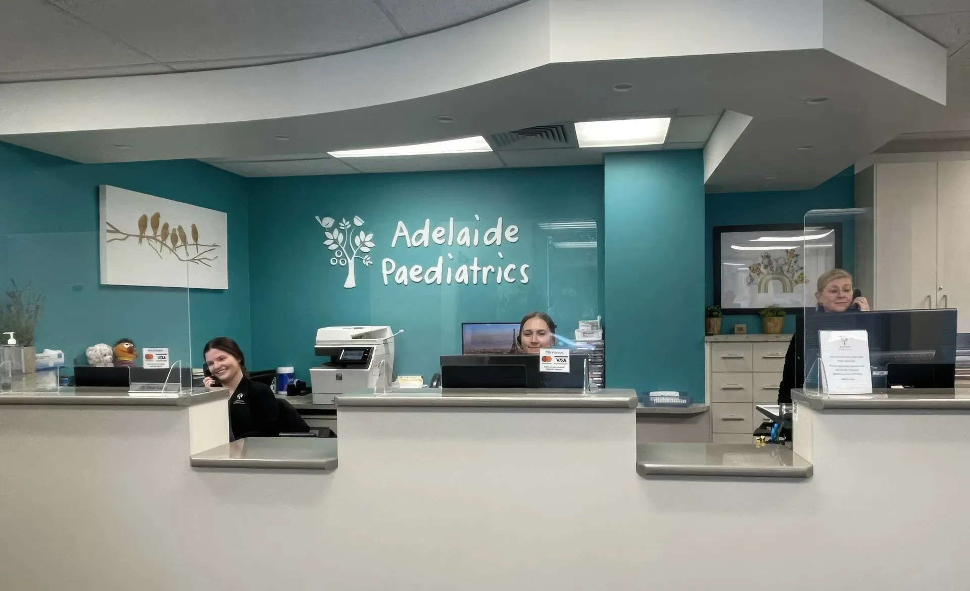 Clinic reception desk with staff behind counters in a teal-walled pediatric office