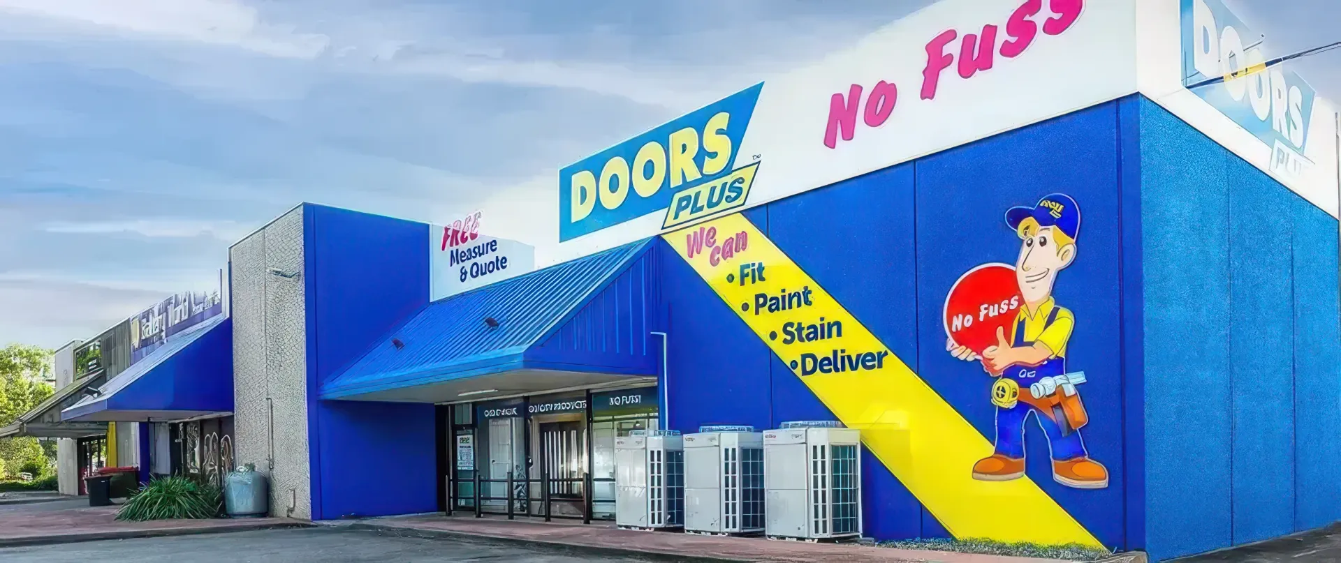 Blue storefront with yellow diagonal stripe, “DOORS” and “No Fuss” signs, and a cartoon mascot near the entrance