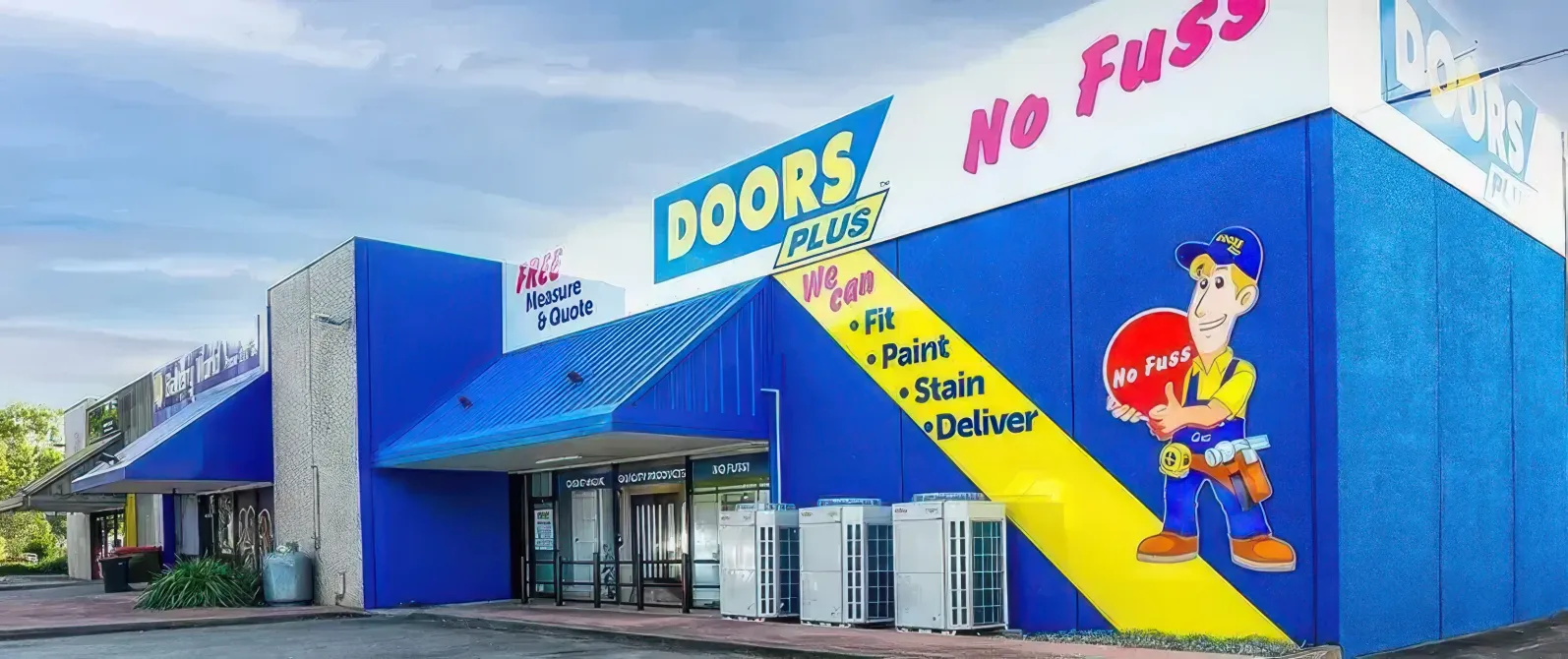 Blue storefront with a yellow mural, “DOORS” and “No Fuss” signage, and a cartoon worker on the wall