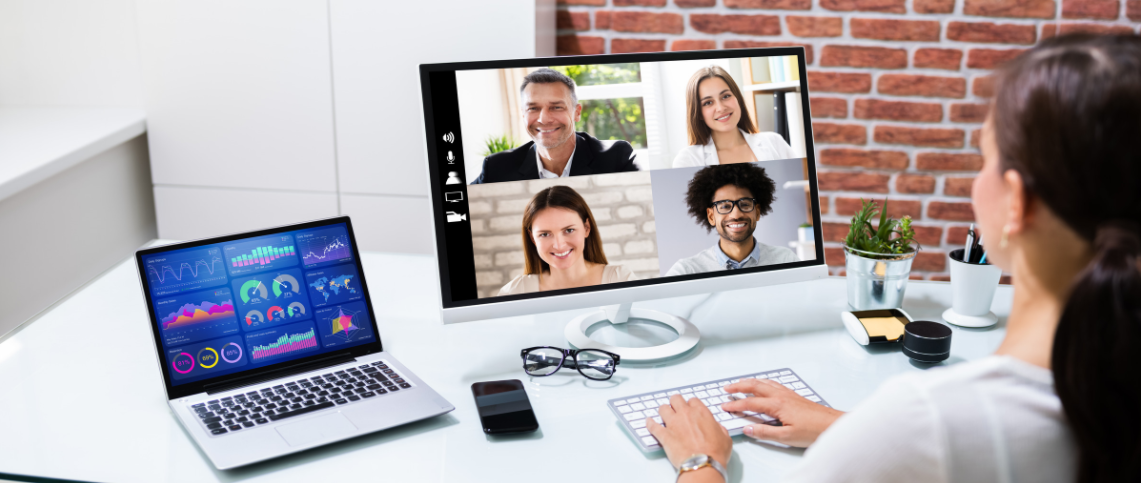 Video conference on a desktop monitor with a laptop and keyboard on a bright office desk