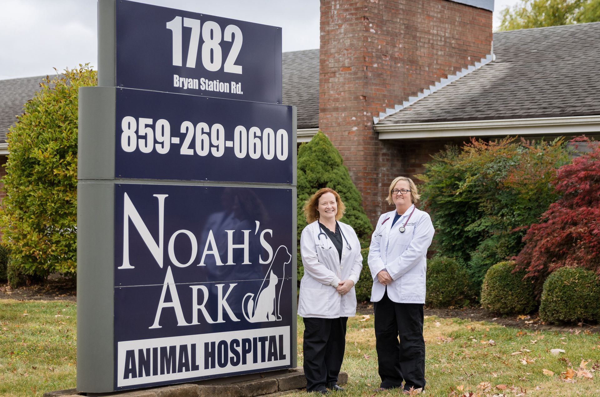 Two doctors standing in front of a noah 's ark animal hospital sign