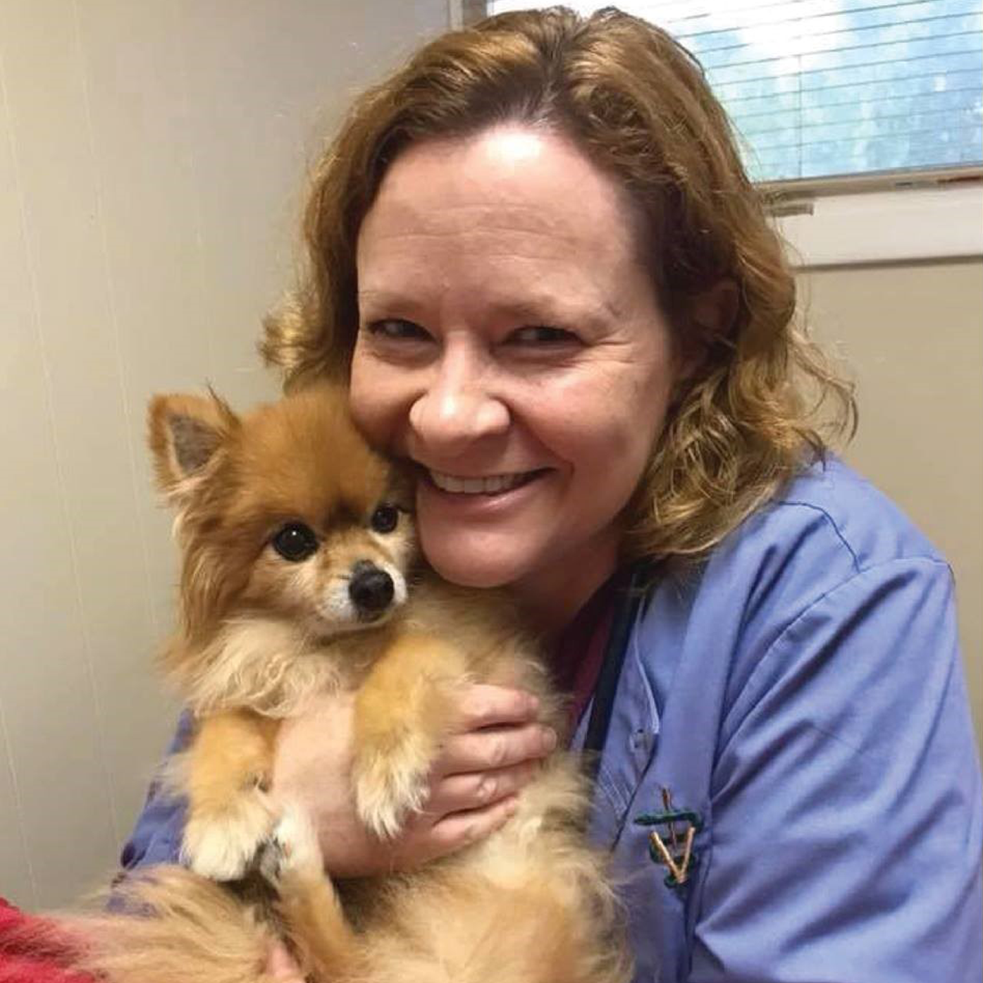 A woman is holding a small dog in her arms and smiling.