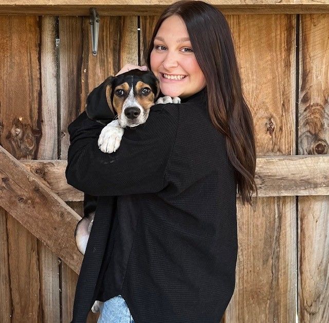 A woman in a black sweater is holding a brown and white dog