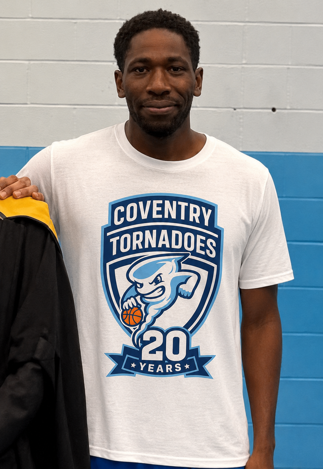 Man standing in a white Coventry Tornadoes T-shirt with a blue team logo and “20 years” graphic.