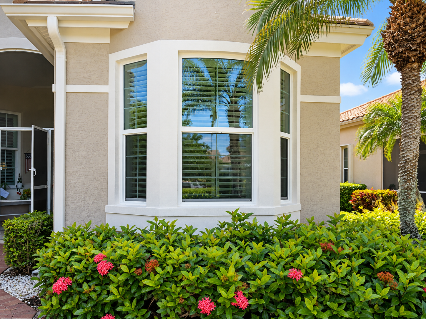 White-framed replacement windows installed on a Florida home with a landscaped exterior