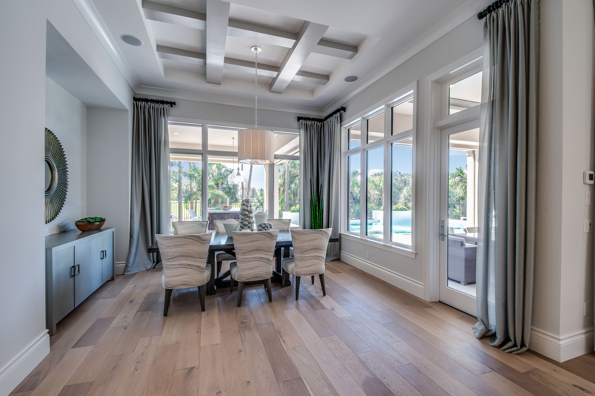 Elegant dining room with a large table, floor-to-ceiling windows, wood floor, and gray curtains.