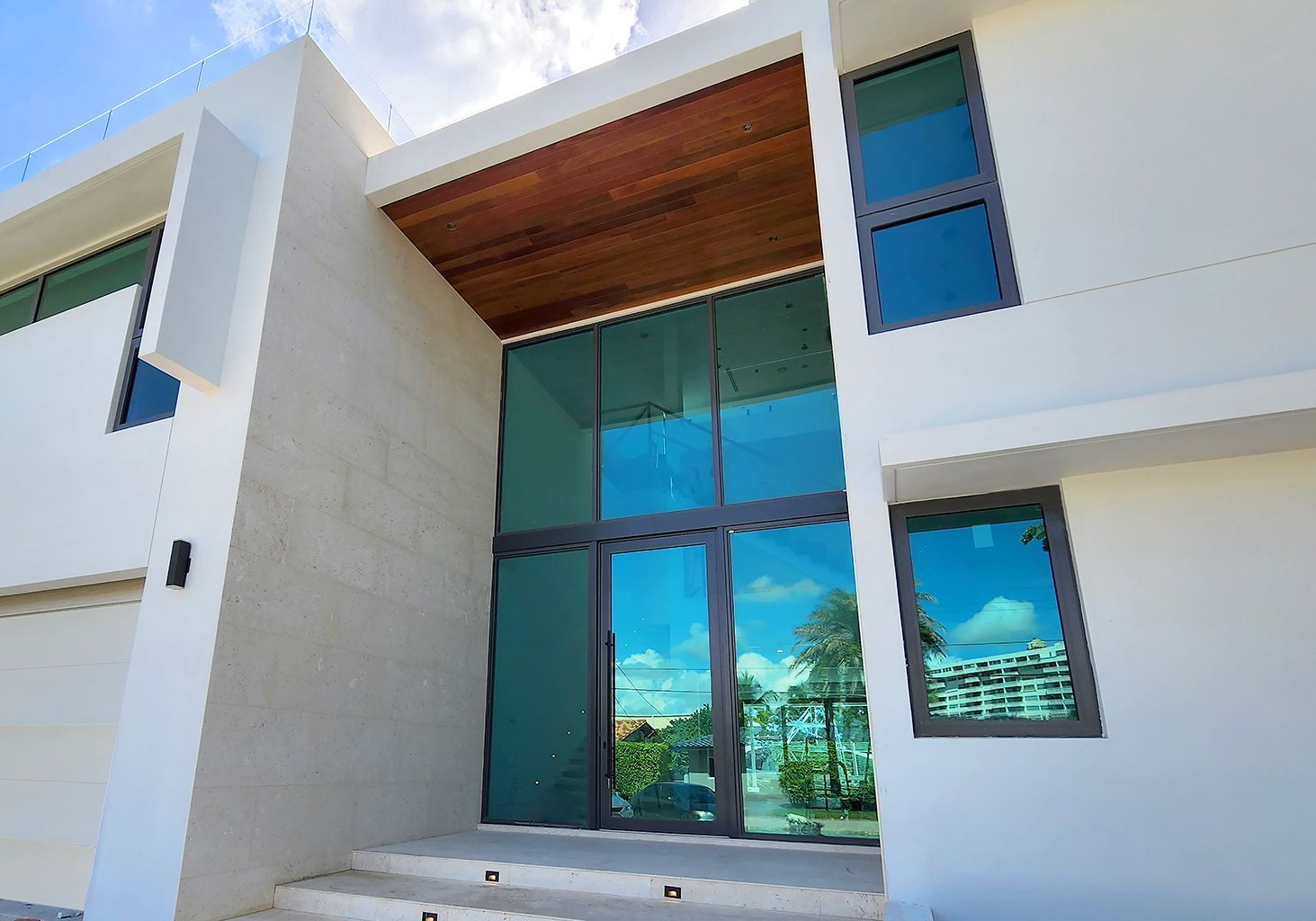 Modern white house with large glass entry doors and wood ceiling detail.