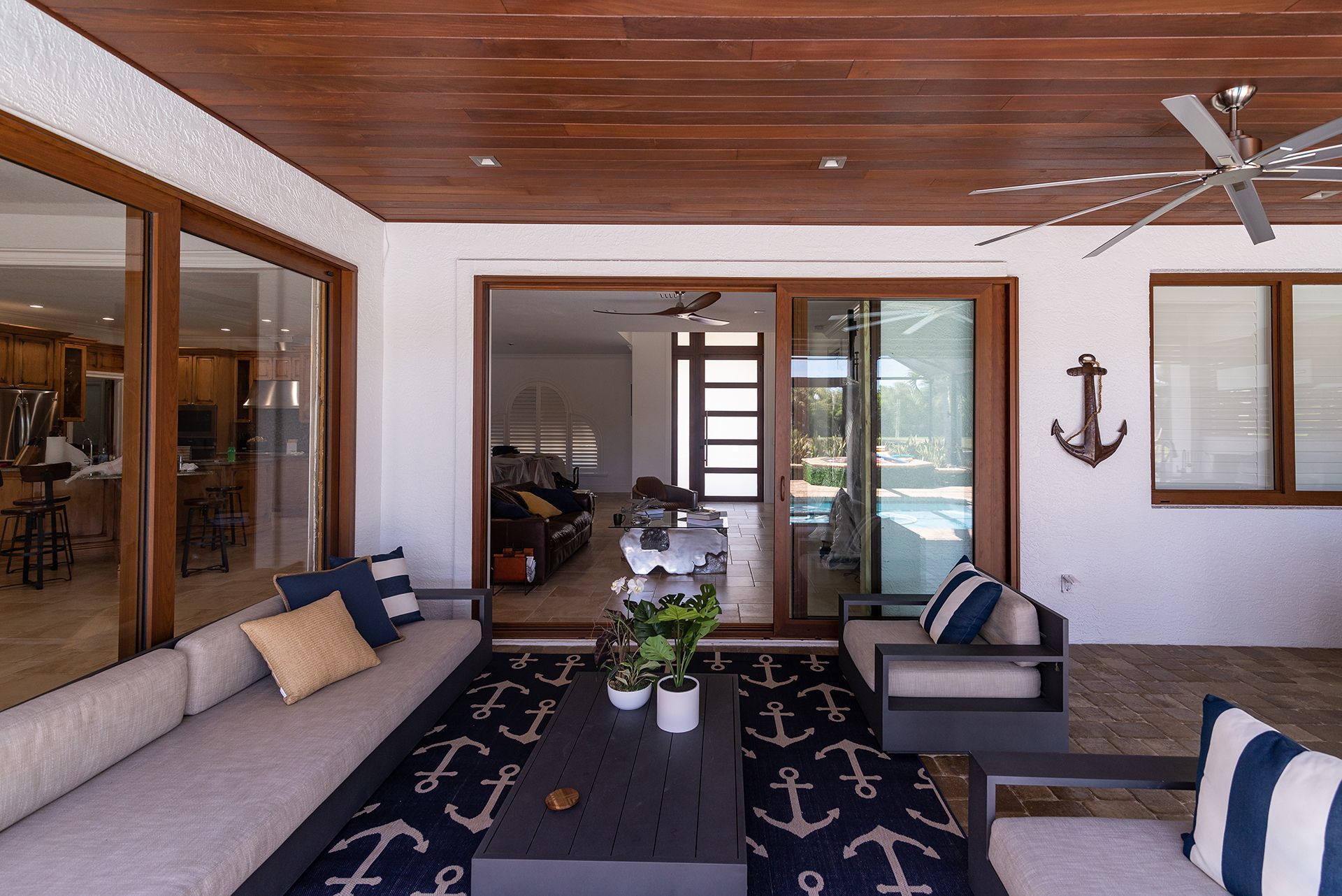 Covered outdoor patio with seating, anchor decor, wood ceiling, and sliding glass doors.