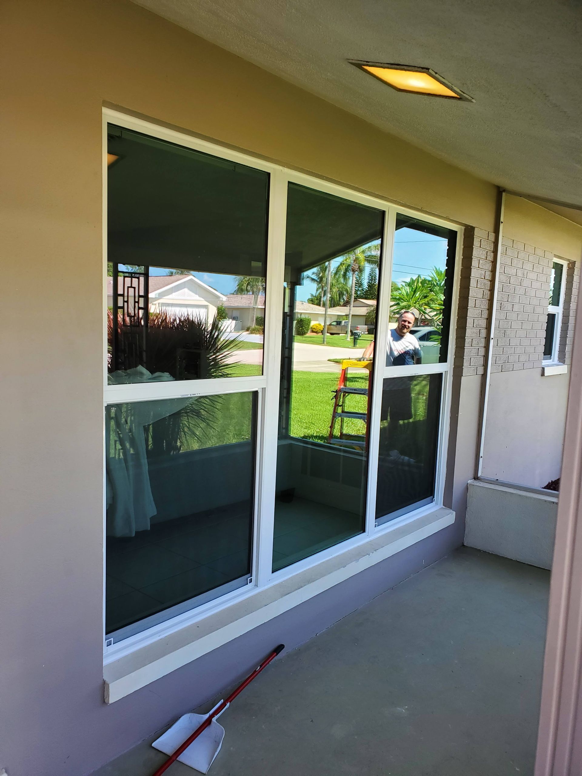Large window with white trim reflects a yard and home; the walls are beige with a hint of a porch.