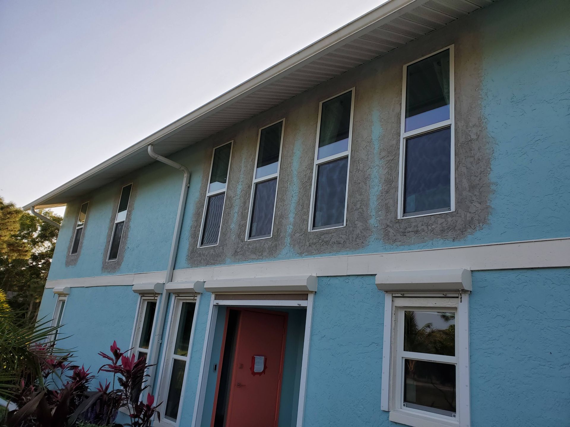 Blue house with window outlines showing patching; white trim; clear sky.