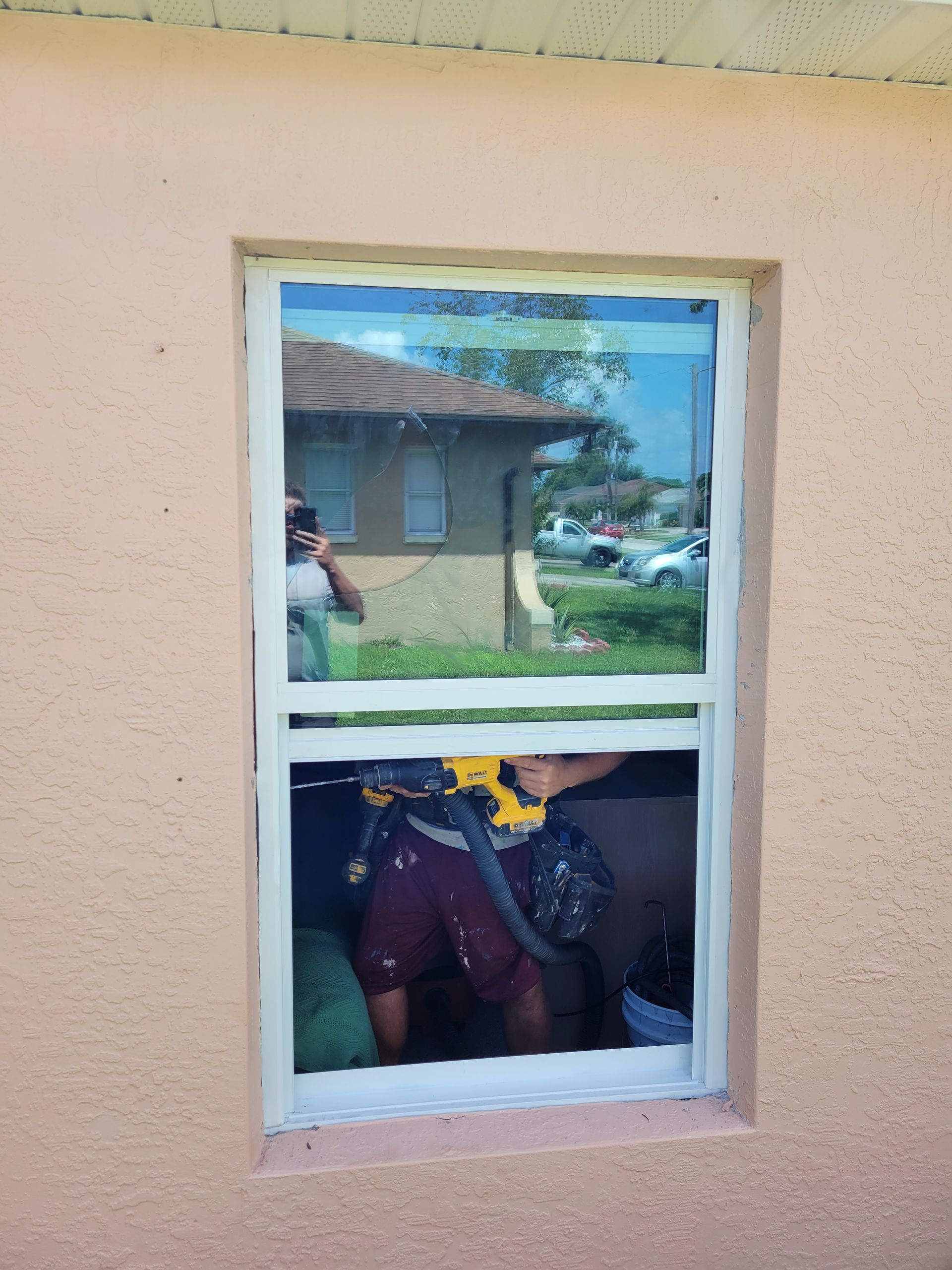 Person installing a window. They are inside, using a drill. The exterior wall is pink.