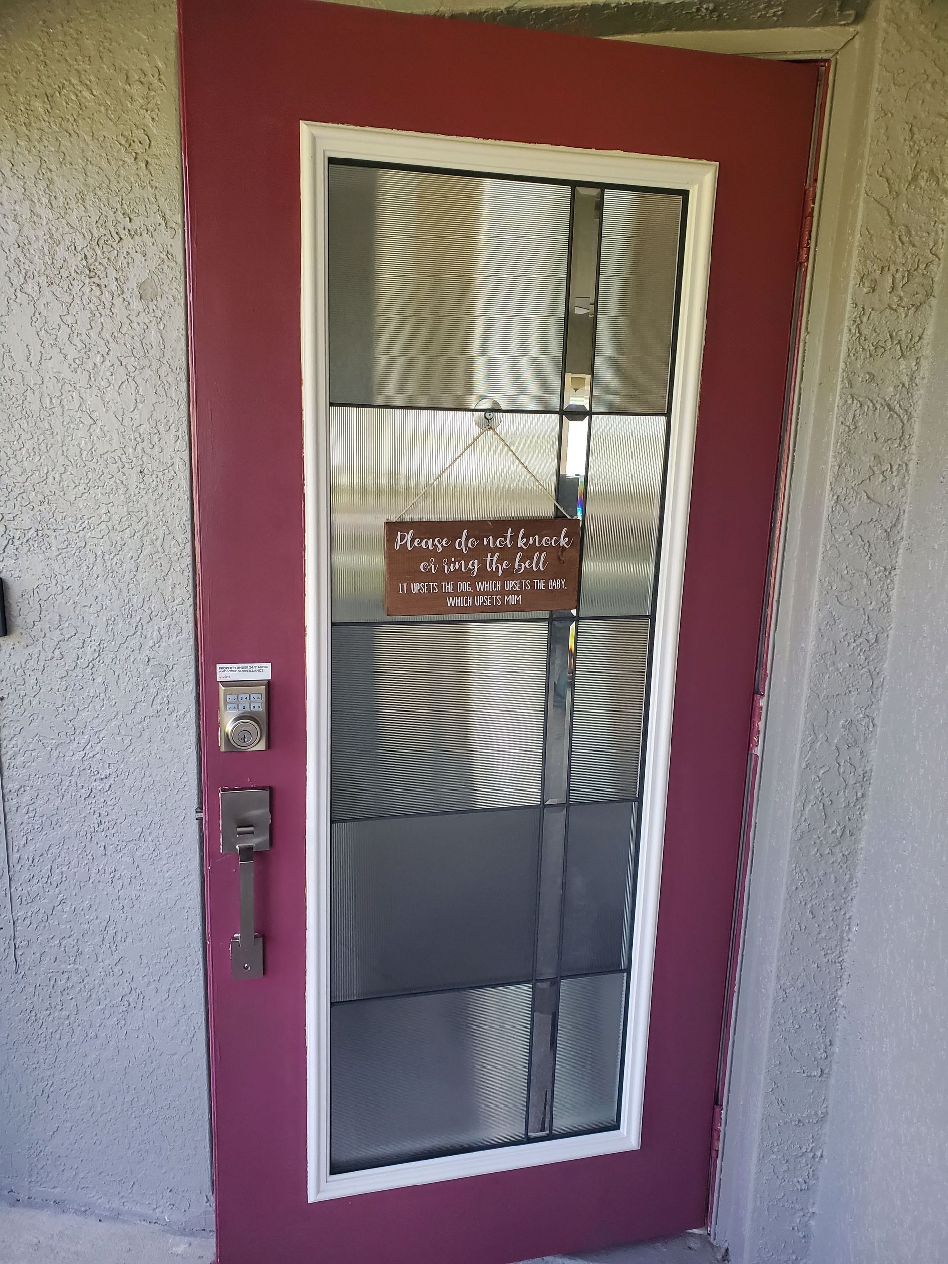 Red door with white trim, screen, and a sign. Silver door handle and lock. Exterior setting.