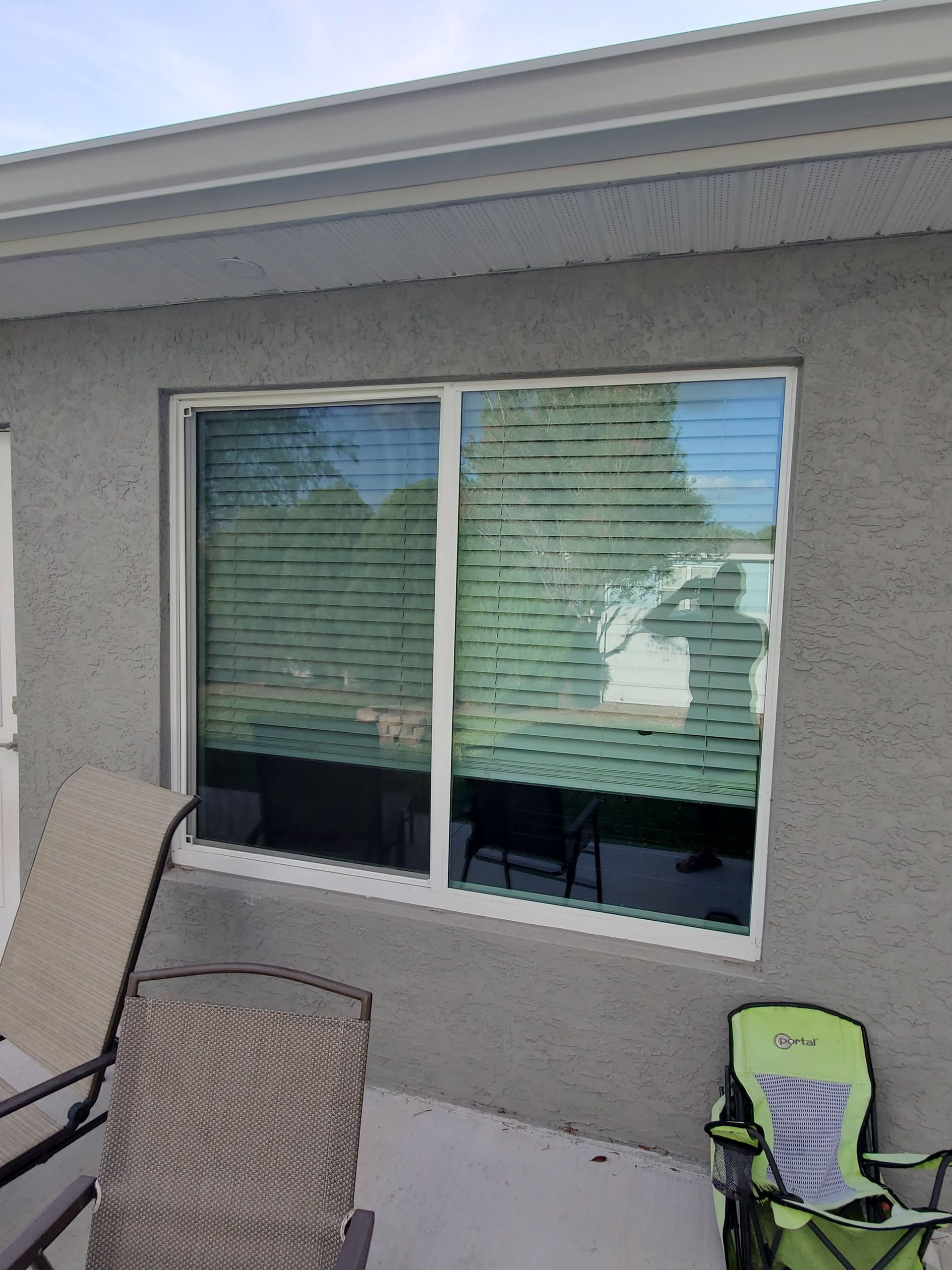 Window with blinds on a stucco wall, with patio chairs in front.