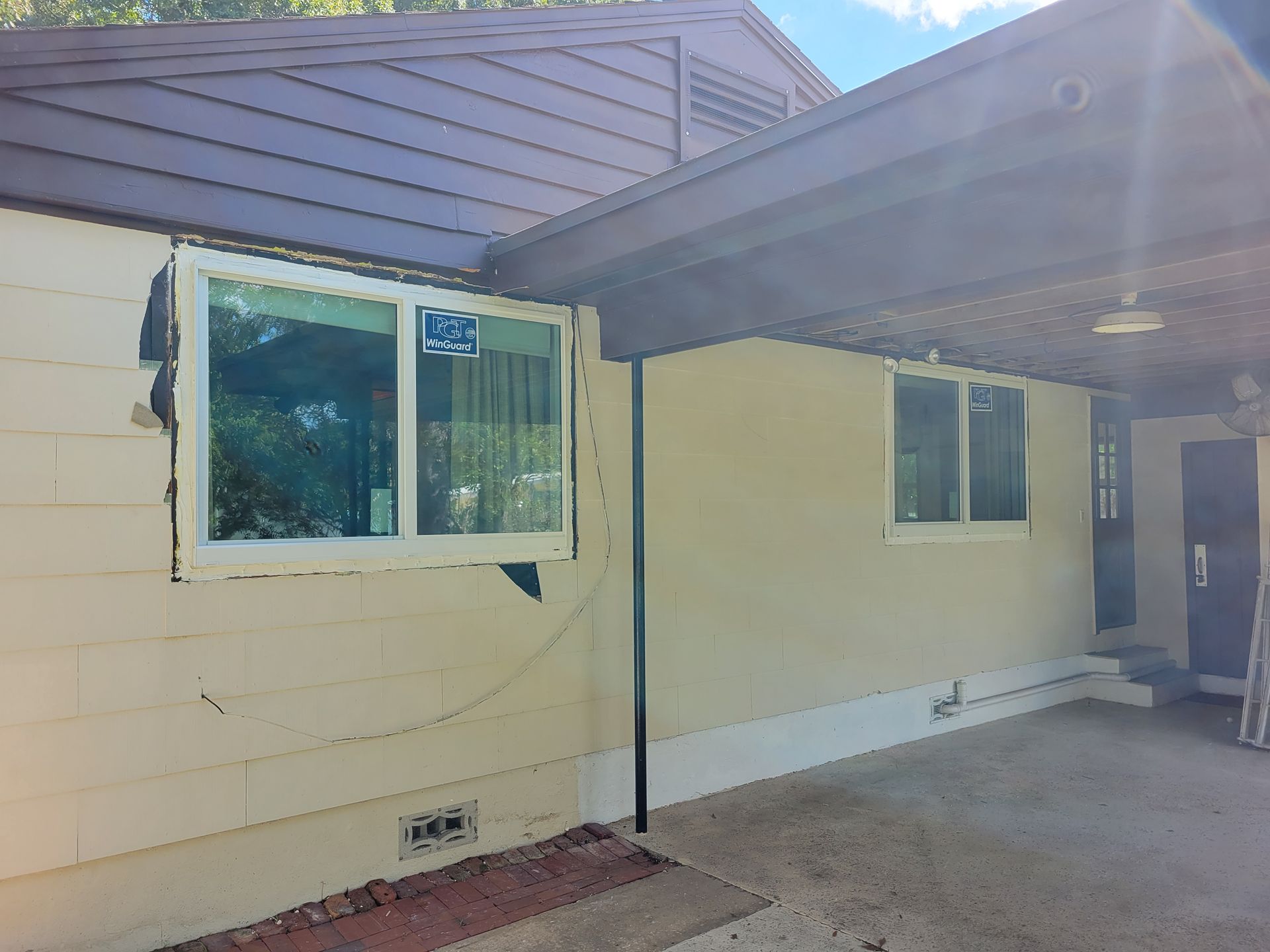 Exterior view of a beige house with a new window installed. A covered carport is on the right.