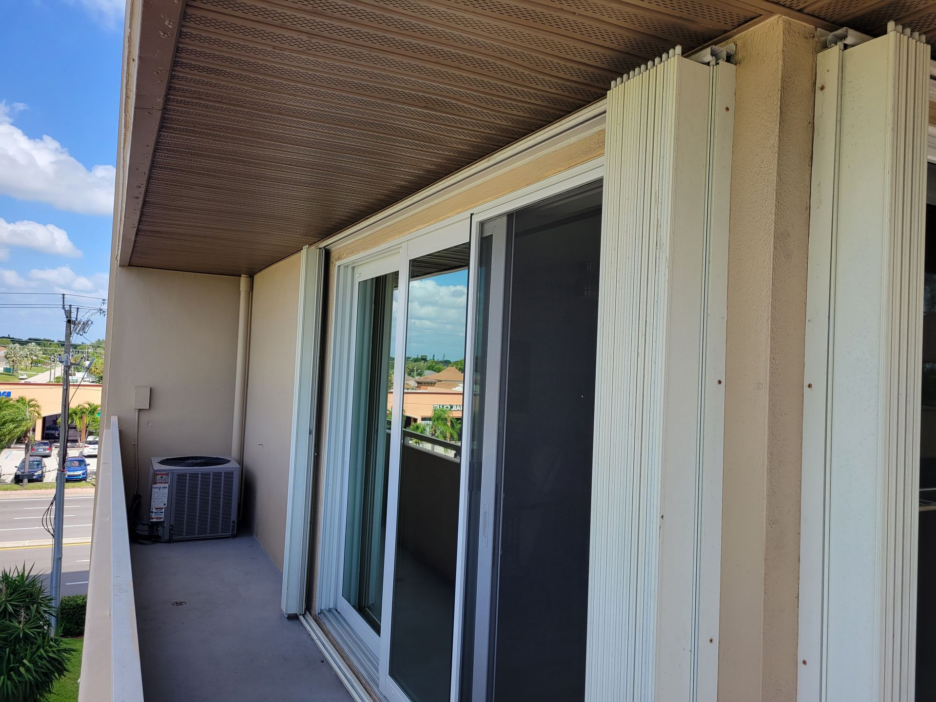 Balcony with sliding glass doors, hurricane shutters, and a view of buildings and a road.