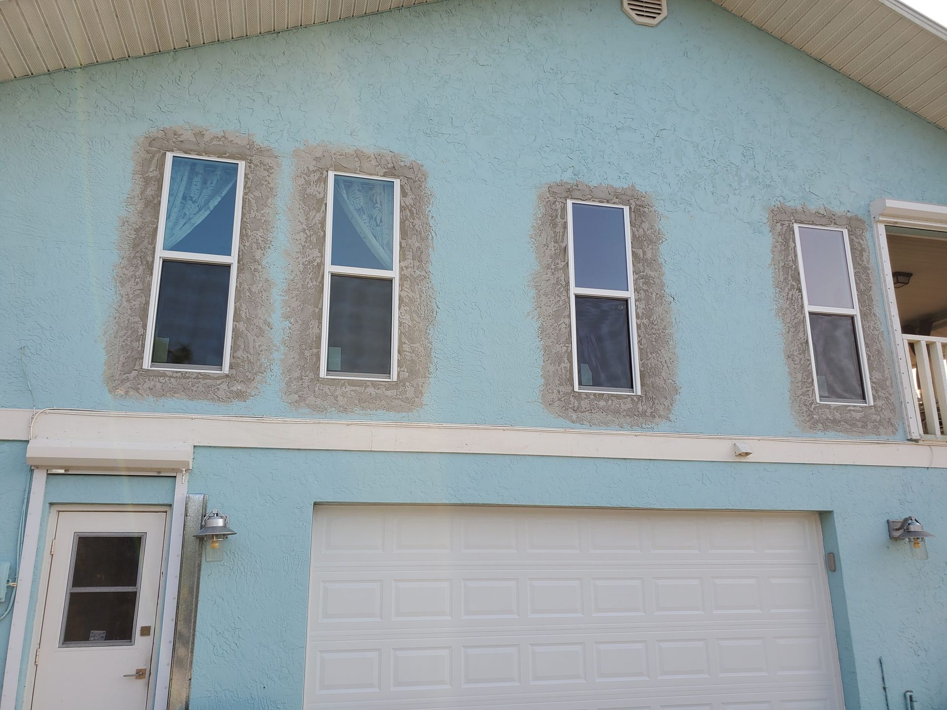 Blue house with white garage door and windows trimmed with textured gray stucco.