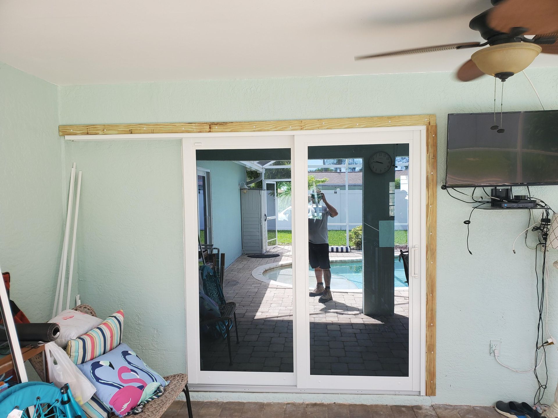 Sliding glass door, partially open, leads to a pool area. A person is reflected in the glass.
