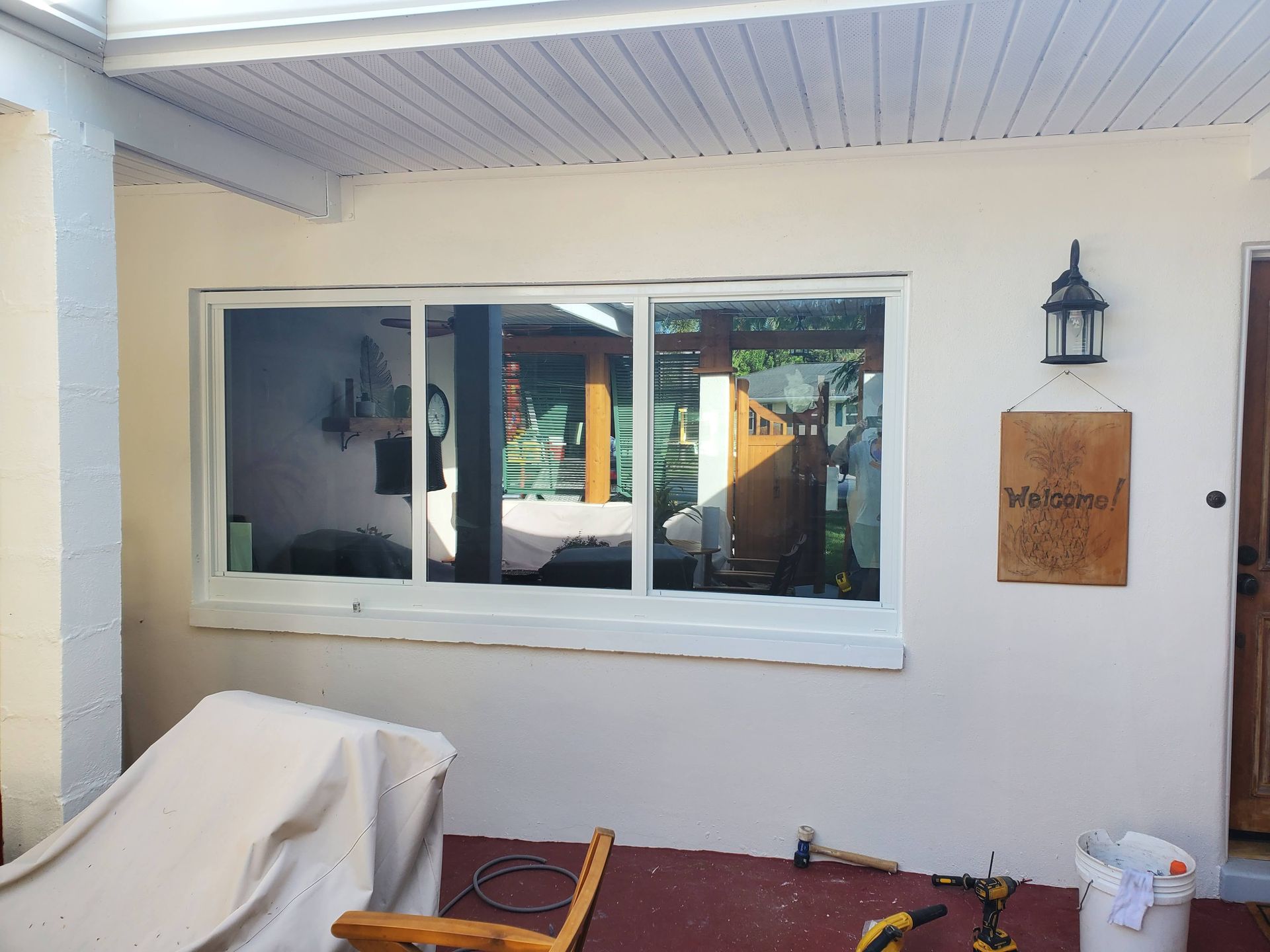 White window on a beige stucco wall, under a white ceiling. A lantern and sign are to the right.