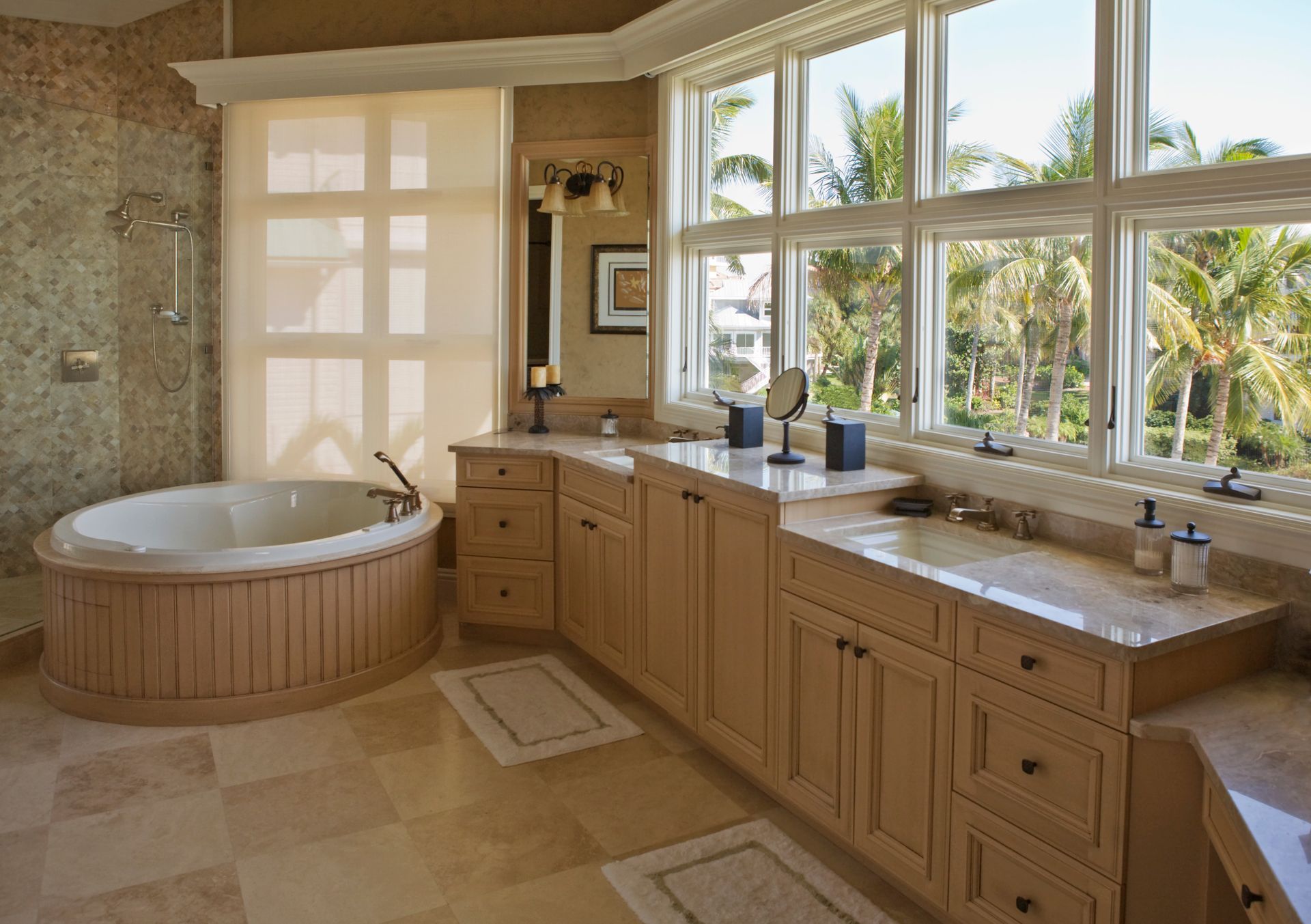 Bathroom with light wood cabinetry, oval tub, and large window with view of palm trees.