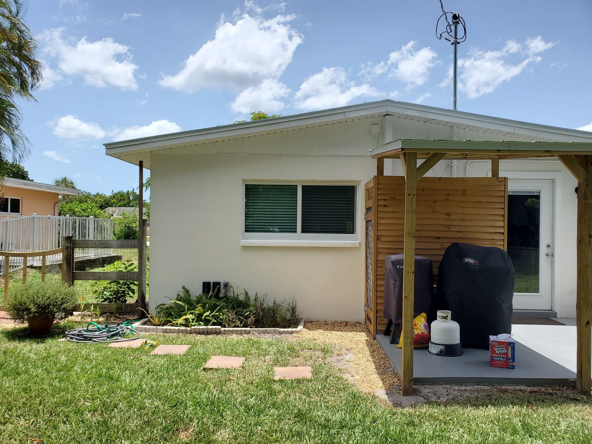 Backyard with small white building, wooden pergola, grill, and green grass.