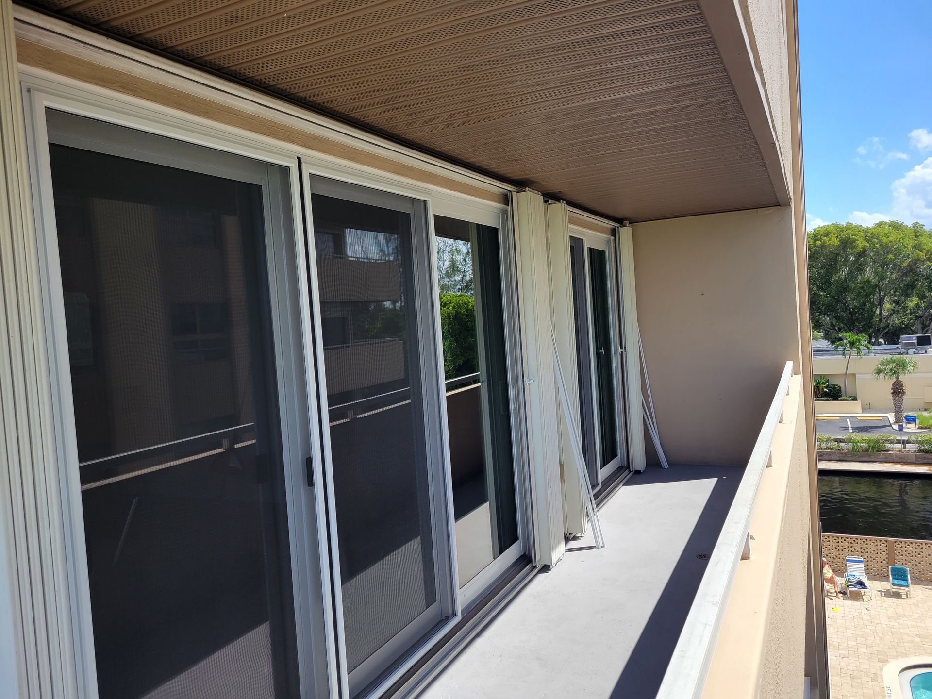 Balcony with sliding glass doors and sheer curtains, overlooking a pool area.