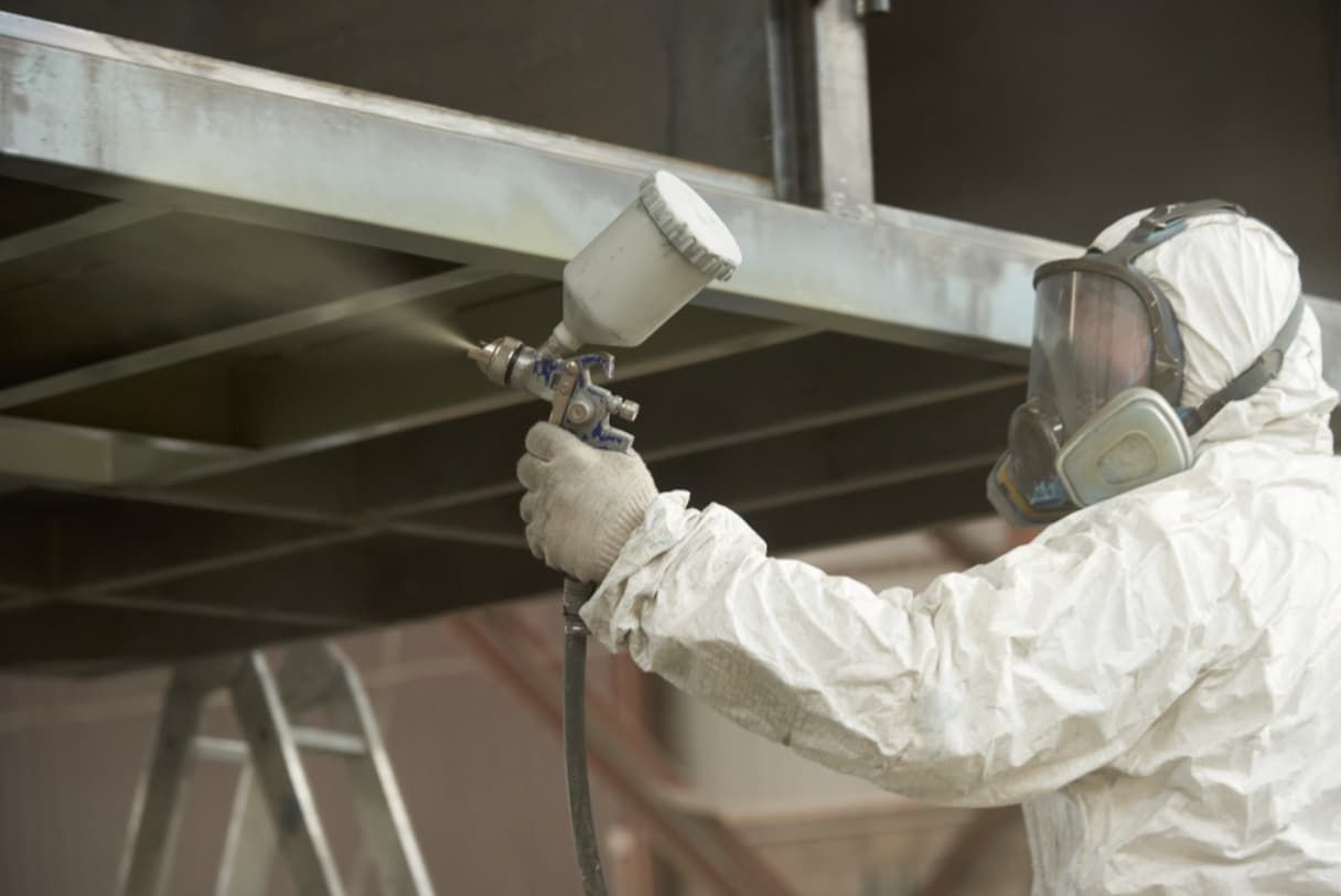 A Man In A Protective Suit Is Spray Painting A Metal Structure — Rockhampton Powdercoating & Fence Panels in Park Avenue, QLD