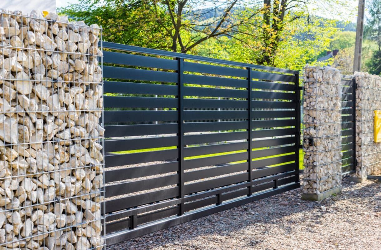 A Black Fence With A Gate Surrounded By Rocks — Rockhampton Powdercoating & Fence Panels in Park Avenue, QLD