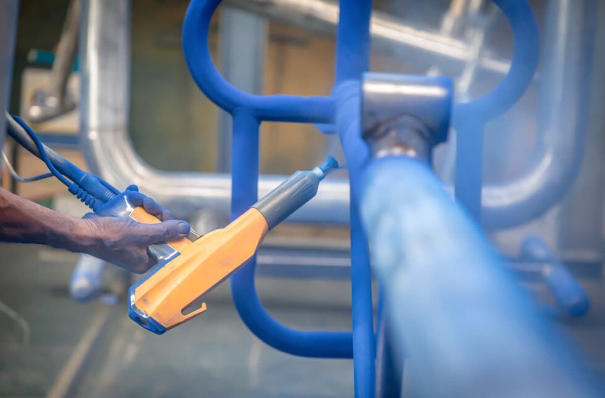 A Person Is Spraying Powder Paint On A Blue Railing — Rockhampton Powdercoating & Fence Panels in Park Avenue, QLD