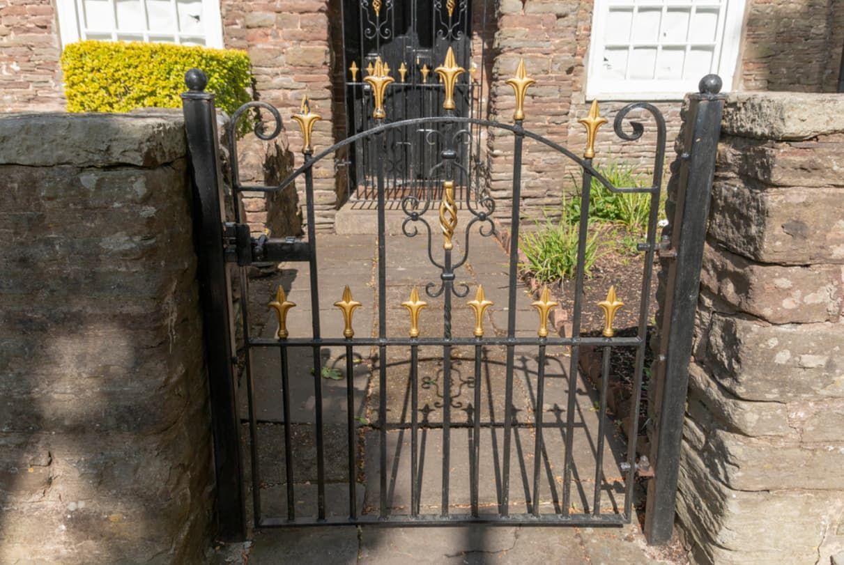 A Wrought Iron Gate With Gold Crosses On It Is In Front Of A Brick Building — Rockhampton Powdercoating & Fence Panels in Park Avenue, QLD