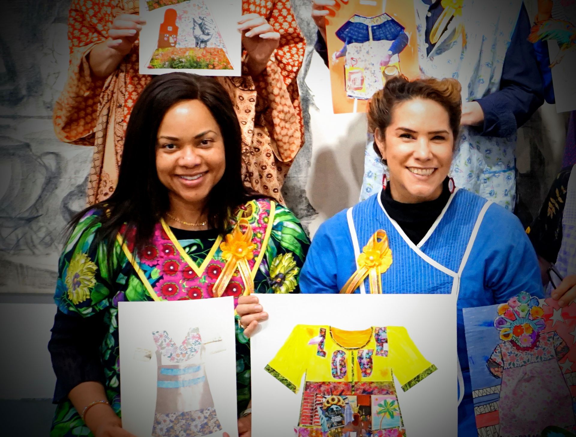 Two people smiling, holding fashion design sketches and colorful T-shirts in a studio setting