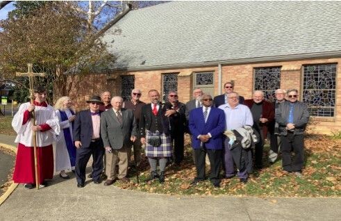 Group of people outside a church. Some are wearing formal attire, a cross is visible.