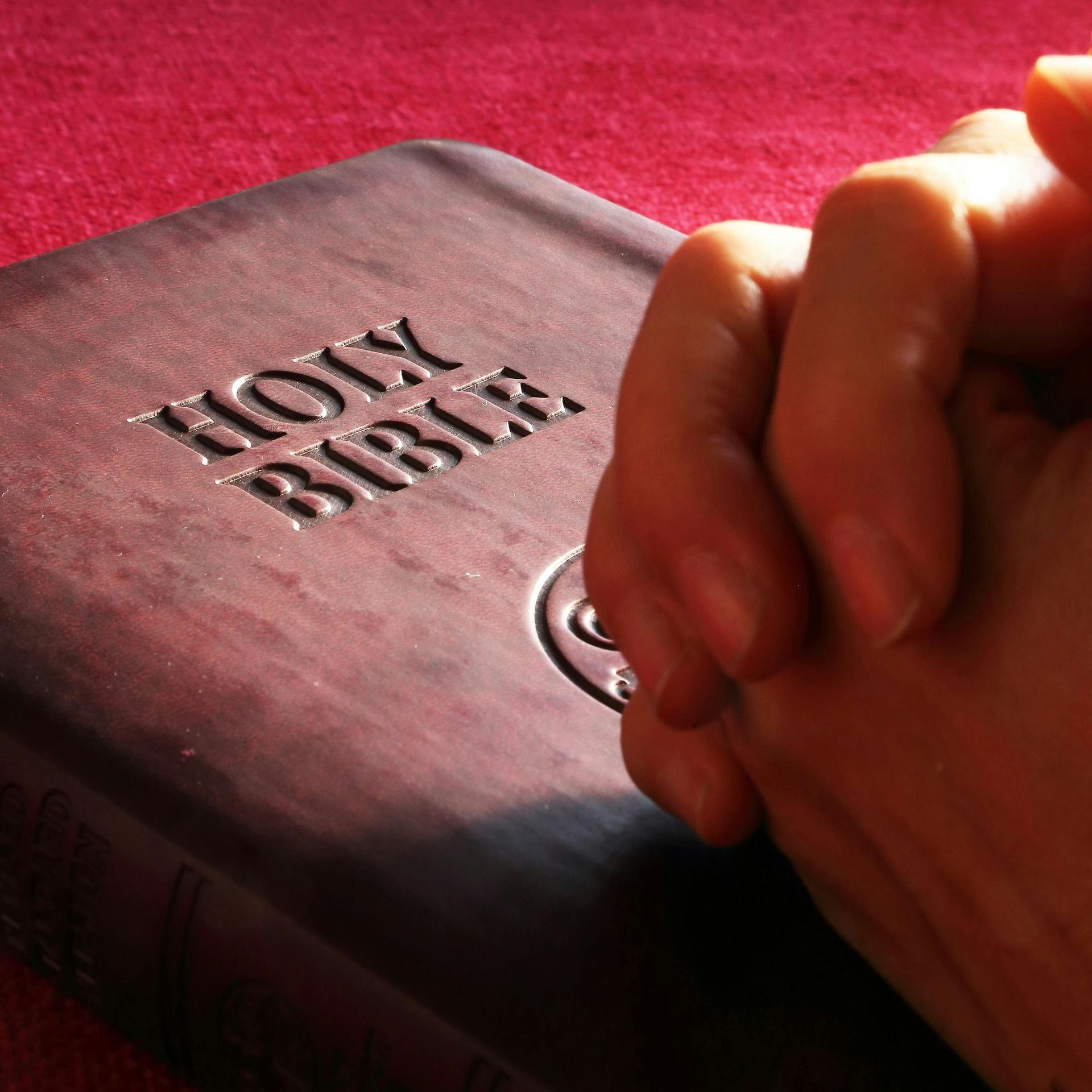 Hands clasped in prayer resting on a closed Bible with